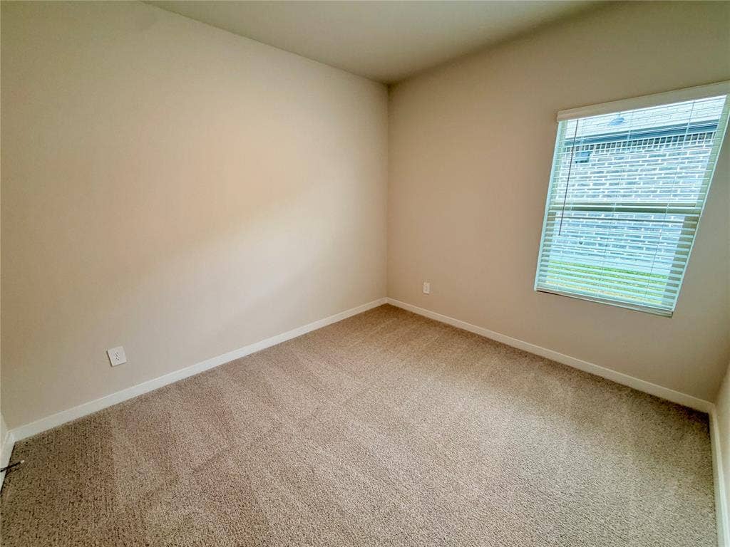 Neutral-toned interior room featuring wall-to-wall carpeting and a single-hung window with horizontal blinds