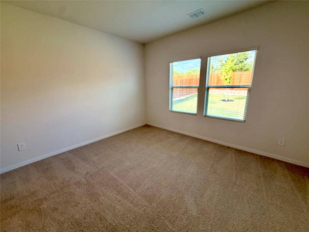 Neutral wall tones, wall-to-wall carpeting, and dual windows providing natural light