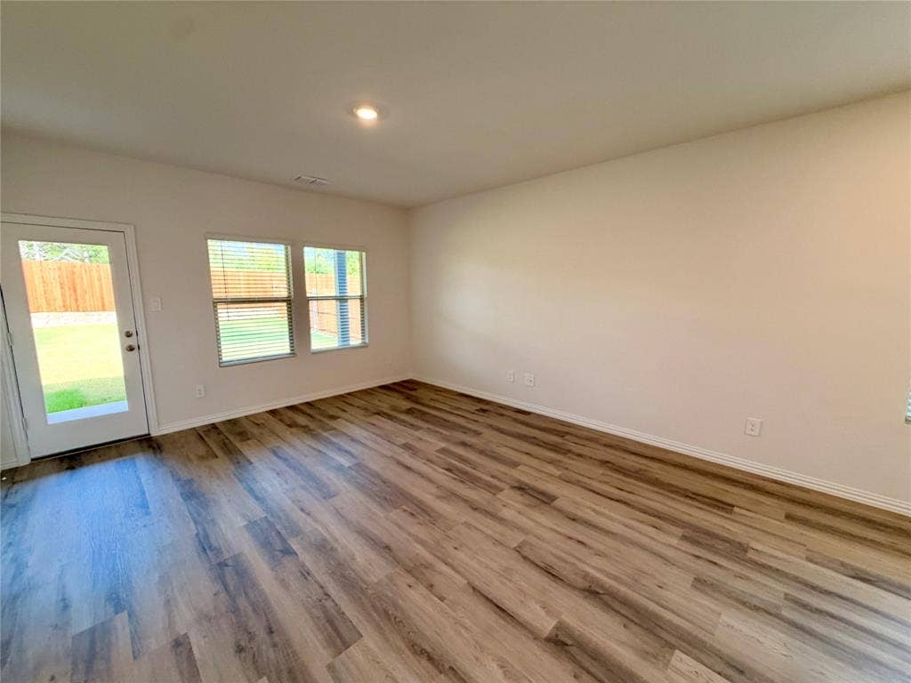 Neutral-toned interior featuring wood-finish flooring, recessed lighting, and double-paned windows with horizontal blinds, complemented by a full-lite glass exterior door
