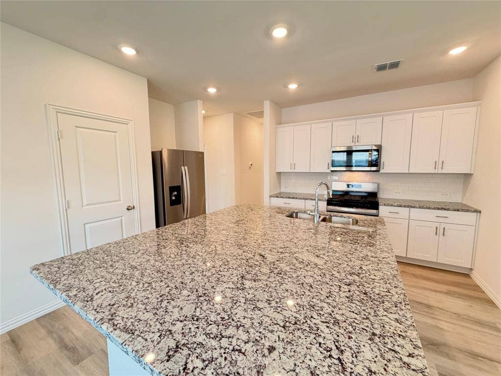 Kitchen featuring a spacious island with a stone countertop, white cabinetry, stainless steel appliances, recessed lighting, and wood-finish flooring