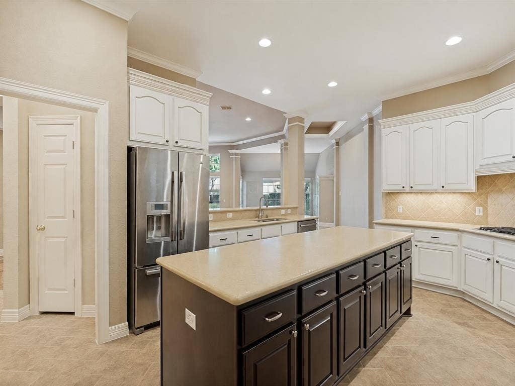 604 Barkley Drive, McKinney, TX 75071 Kitchen featuring white upper cabinetry, contrasting dark-toned center island with quartz countertop, stainless steel refrigerator, tile backsplash, and neutral-toned flooring