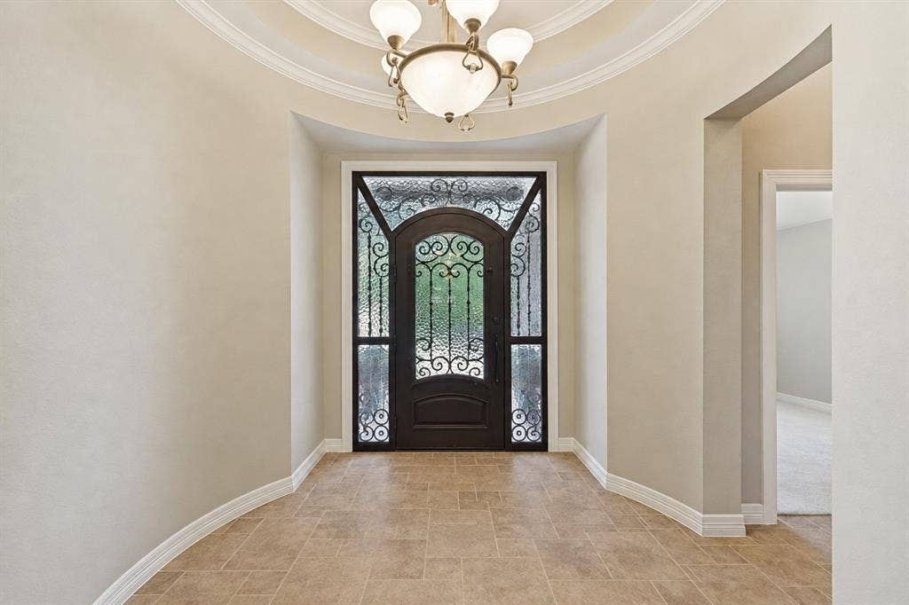 604 Barkley Drive, McKinney, TX 75071 Entryway featuring a rotunda ceiling with crown molding, a central multi-arm chandelier, large-format tile flooring, and an arched entryway door with decorative wrought-iron detailing and textured glass panels