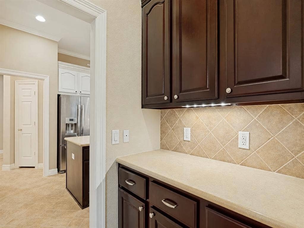 604 Barkley Drive, McKinney, TX 75071 Dark-finish cabinetry with silver-tone hardware, stone-composite countertop, and diagonal-pattern tile backsplash