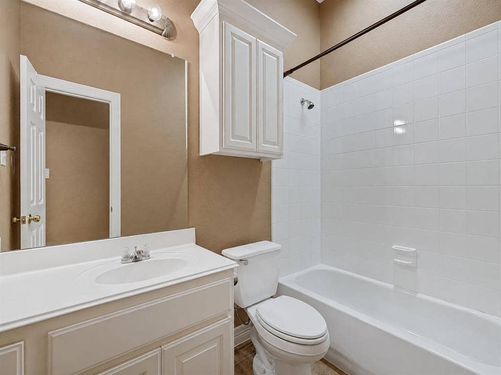 604 Barkley Drive, McKinney, TX 75071 Bathroom featuring a white vanity cabinet with an integrated sink, a wall-mounted storage cabinet with crown molding, a frameless vanity mirror, and a tub-shower combination with white tiled wall surrounds
