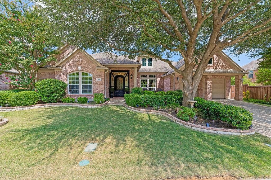 604 Barkley Drive, McKinney, TX 75071 Brick exterior with a multi-gabled roofline, arched window detailing, an arched front entryway with leaded glass door, and a curved stone-edged landscape bed