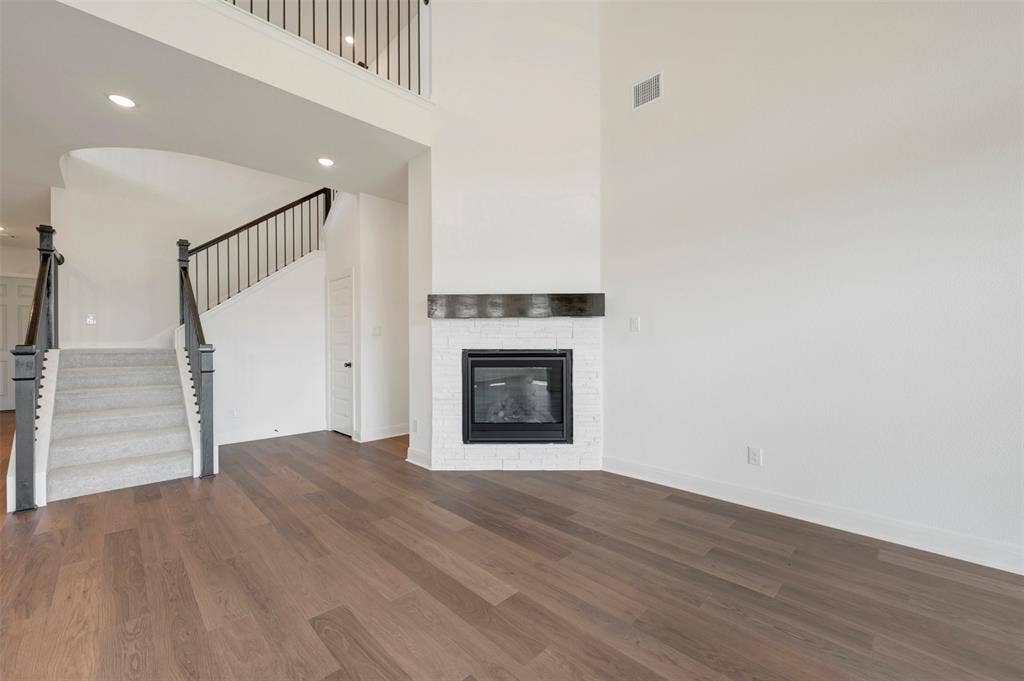 3469 Jersey Drive, Midlothian, TX 76065 High-ceiling interior featuring wood-finish flooring, a white painted brick fireplace with a dark timber mantel, a staircase with metal balusters, and recessed lighting