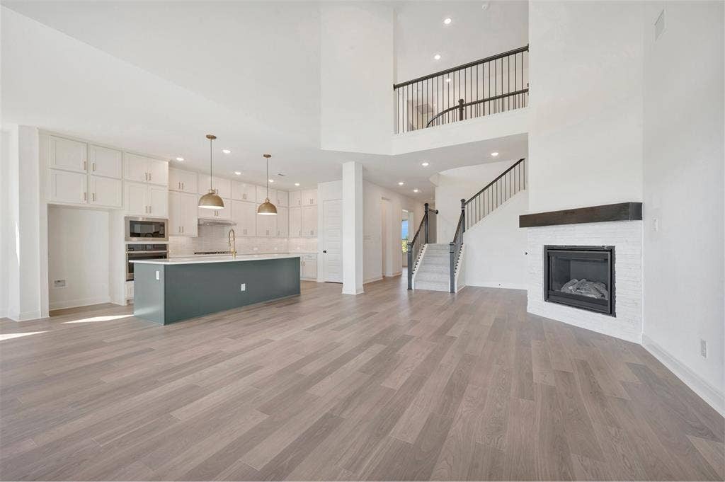 3469 Jersey Drive, Midlothian, TX 76065 Open-concept interior featuring wood-finish flooring, a kitchen island with pendant lighting, built-in wall cabinetry, a fireplace with a masonry surround and dark mantel, and a staircase with decorative metal balusters