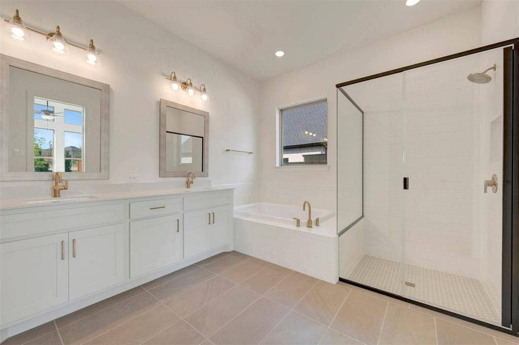 3469 Jersey Drive, Midlothian, TX 76065 Bathroom featuring a double vanity with stone countertops, a tiled walk-in shower with a glass enclosure, a deep soaking tub, and brass-tone fixtures