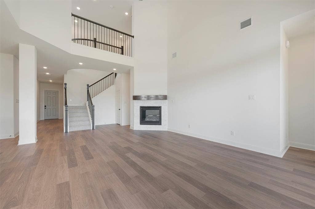 3469 Jersey Drive, Midlothian, TX 76065 Two-story living area featuring vaulted ceilings, wood-finish flooring, a fireplace with a light-colored surround and dark wood mantel, and a staircase with a metal railing