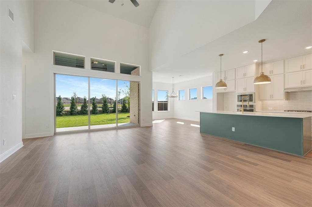 3469 Jersey Drive, Midlothian, TX 76065 Vaulted ceilings with expansive floor-to-ceiling glass sliding doors, wood-finish flooring, kitchen island with quartz-surface countertop, and custom cabinetry with built-in stainless steel appliances