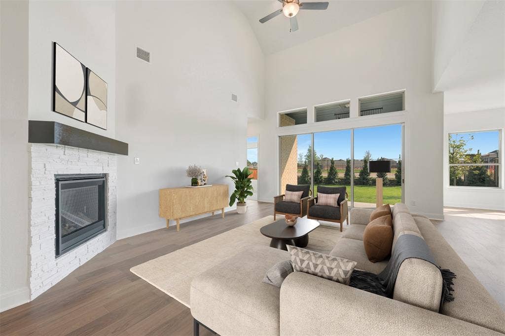 3469 Jersey Drive, Midlothian, TX 76065 Vaulted ceiling with an integrated fan, floor-to-ceiling fireplace with painted brick finish and a prominent mantel, wood-finish flooring, and expansive windows featuring transom lights