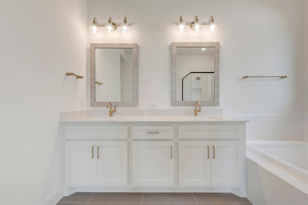 3469 Jersey Drive, Midlothian, TX 76065 Double vanity featuring white cabinetry, a light-toned solid surface countertop, integrated dual sinks with metal fixtures, framed vanity mirrors, and three-light wall-mounted sconces