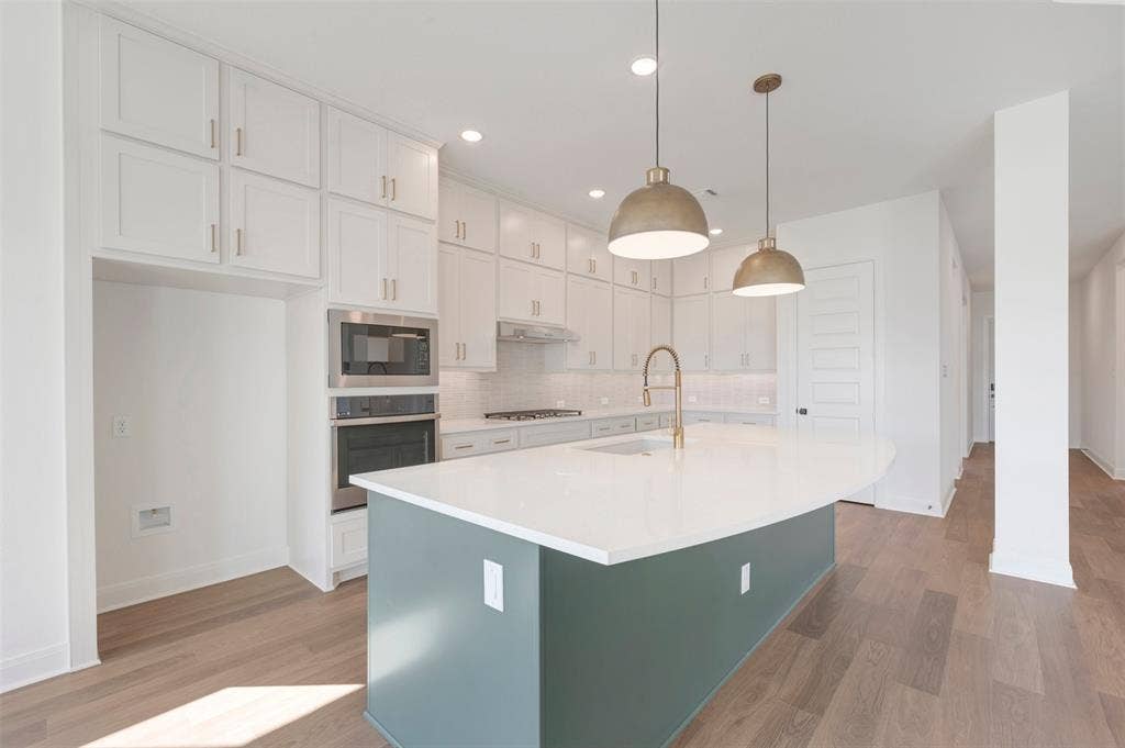3469 Jersey Drive, Midlothian, TX 76065 Kitchen featuring floor-to-ceiling white cabinetry, a center island with a solid-surface countertop, wood-finish flooring, built-in stainless steel appliances, and dual dome pendant lighting