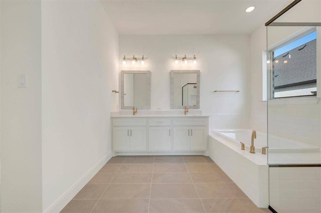 3469 Jersey Drive, Midlothian, TX 76065 Double vanity with white cabinetry, rectangular drop-in sinks, brass-toned fixtures, wall-mounted rectangular mirrors, and a deep soaking tub