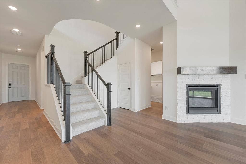 3469 Jersey Drive, Midlothian, TX 76065 Staircase with wooden handrails and balusters, wood-finish flooring, recessed lighting, and a white-painted brick fireplace featuring a dark wood mantel