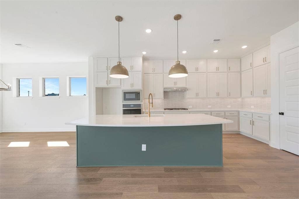 3469 Jersey Drive, Midlothian, TX 76065 Kitchen featuring a center island with a solid surface countertop, white shaker-style cabinetry, wood-finish flooring, two metallic pendant lights, and a built-in wall oven and microwave