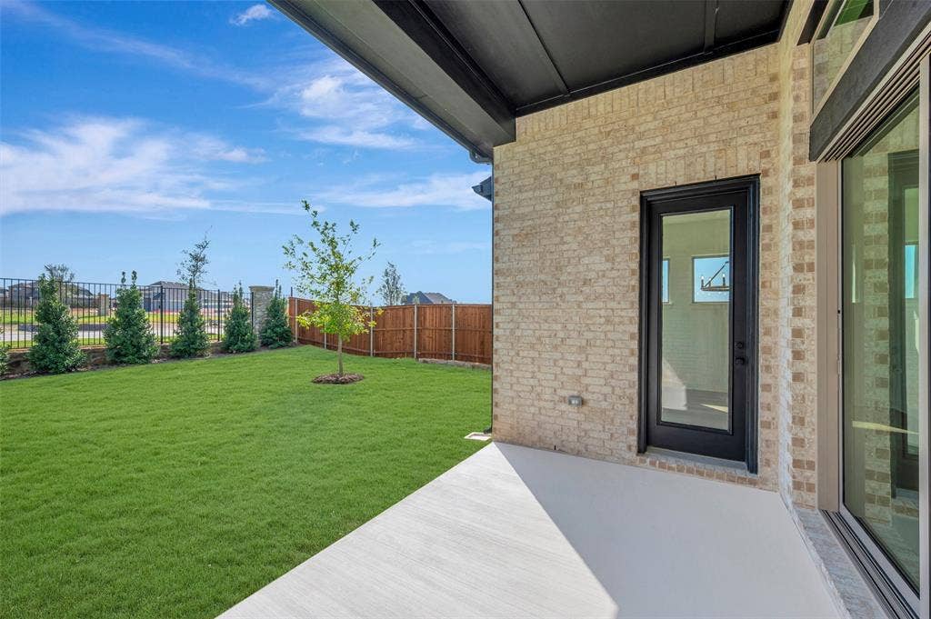 3469 Jersey Drive, Midlothian, TX 76065 Covered concrete patio with light-colored brick exterior, metal roofline, black-framed glass door, and full-pane sliding glass door overlooking a fenced rear yard