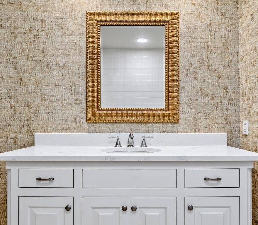 8629 Edgemere Road, #13, Dallas, TX 75225 White cabinetry vanity featuring a stone countertop, an integrated oval sink, a three-piece chrome faucet, and textured wall covering, accented by a decorative metallic framed mirror