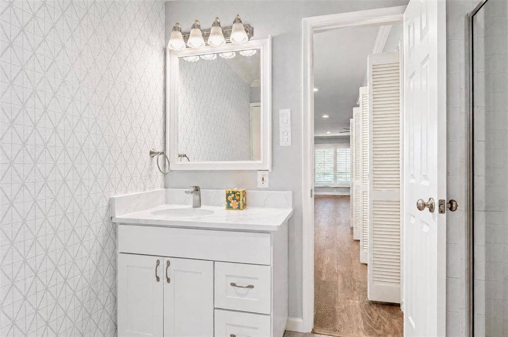 8629 Edgemere Road, #13, Dallas, TX 75225 White vanity with stone countertop, undermount sink, geometric patterned wall covering, four-light vanity fixture, and framed wall mirror