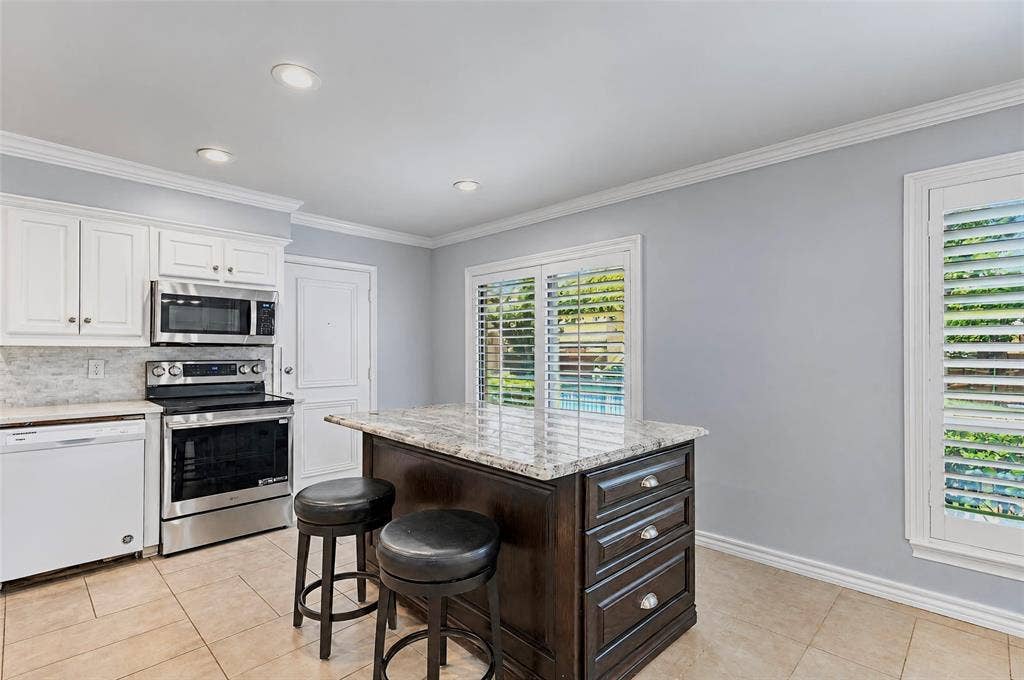 8629 Edgemere Road, #13, Dallas, TX 75225 Kitchen featuring a central island with stone countertop, white shaker-style cabinetry, stainless steel appliances, tile flooring, and plantation shutters