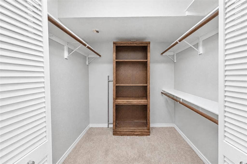 8629 Edgemere Road, #13, Dallas, TX 75225 Walk-in storage space featuring built-in wood shelving, dual-level garment rods, and louvered double-door entry