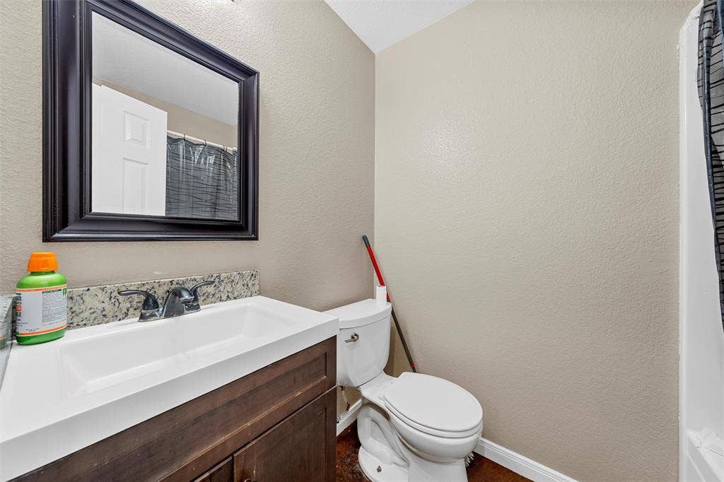 2125 Burnett Avenue, Waco, TX 76706 Unit B Vanity featuring a rectangular basin, natural stone countertop, and dark wood-finish cabinetry, paired with a framed wall mirror and double-handle faucet