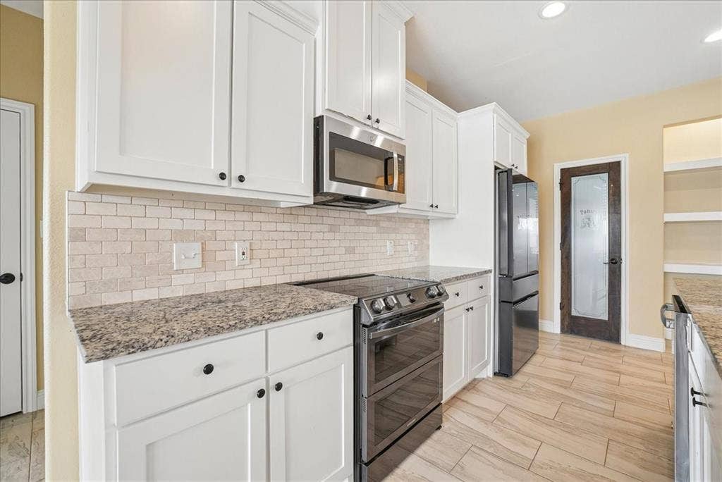 9060 Mitchell Bend Court, Granbury, TX 76048 White shaker-style cabinetry, stone-finish countertops, subway tile backsplash, stainless steel appliances, and wood-finish tile flooring