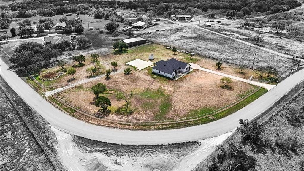 9060 Mitchell Bend Court, Granbury, TX 76048 Aerial perspective of a corner lot featuring an expansive yard, concrete driveway, detached storage structure, and mature trees