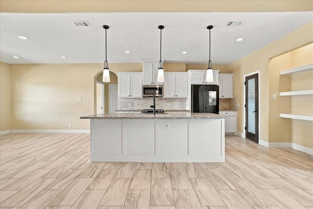 9060 Mitchell Bend Court, Granbury, TX 76048 Kitchen featuring white shaker-style cabinetry, a stone-surfaced center island with an integrated sink, three overhead pendant lights, and light wood-finish tile flooring