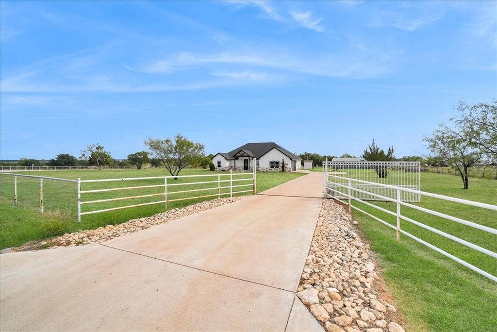 9060 Mitchell Bend Court, Granbury, TX 76048 Concrete driveway with gravel bordering, expansive fenced acreage, and gated entrance