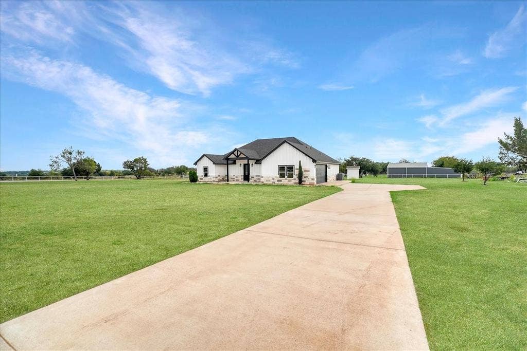 9060 Mitchell Bend Court, Granbury, TX 76048 Single-story residence featuring stone and siding exterior, multi-gabled roofline, concrete driveway, and expansive lawn