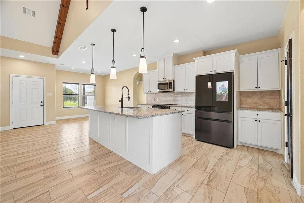 9060 Mitchell Bend Court, Granbury, TX 76048 Kitchen featuring an expansive center island with a stone-finish countertop, white shaker-style cabinetry, a vaulted ceiling with exposed wood beam detail, and large-format tile flooring