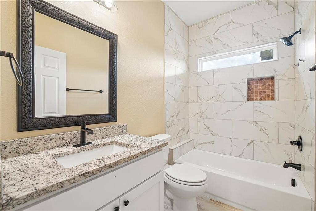 9060 Mitchell Bend Court, Granbury, TX 76048 Bathroom featuring a vanity with stone-finish countertop, white cabinetry, rectangular under-mount sink, matte black fixtures, and a shower-tub combination with tiled surround and built-in niche