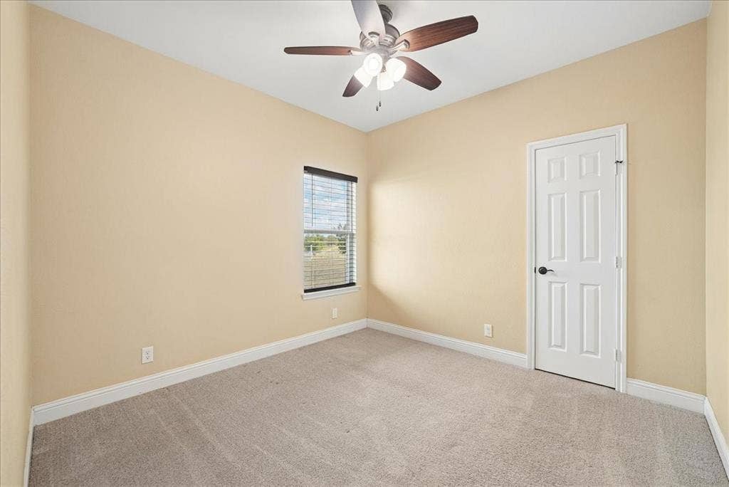 9060 Mitchell Bend Court, Granbury, TX 76048 Neutral-toned interior space featuring neutral wall paint, wall-to-wall carpeting, a six-panel interior door, a single-pane window, and a multi-blade ceiling fan with an integrated light fixture