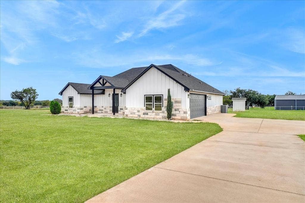9060 Mitchell Bend Court, Granbury, TX 76048 Exterior featuring board and batten siding, stone masonry wainscoting, a covered front entry, and a concrete driveway