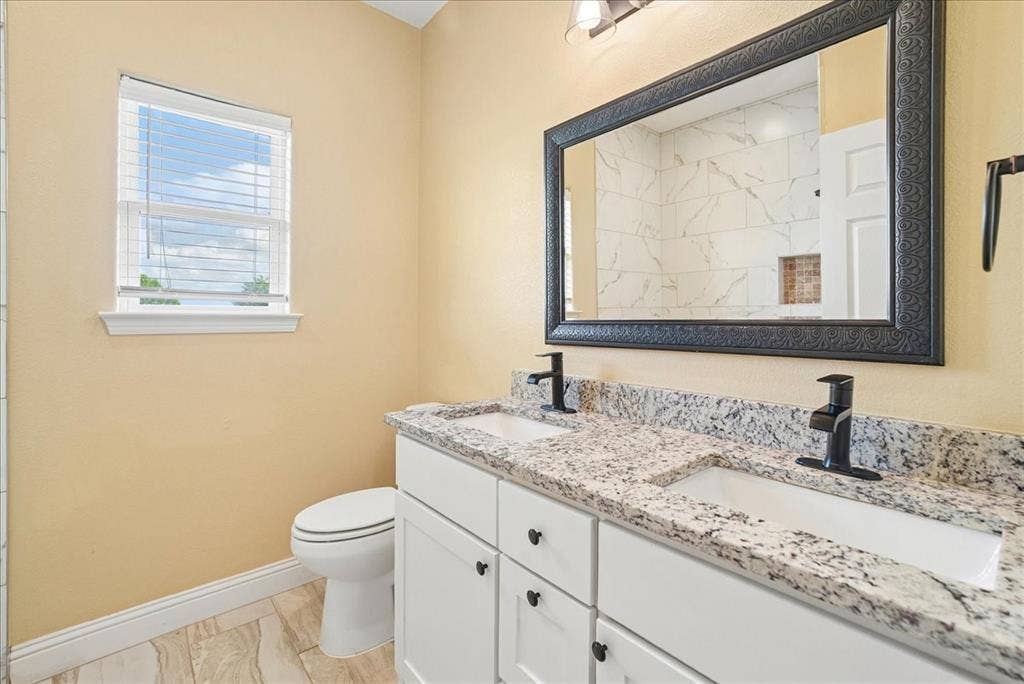 9060 Mitchell Bend Court, Granbury, TX 76048 Double vanity featuring stone countertops, dual under-mount sinks, matte black faucets, white shaker-style cabinetry, and a framed mirror