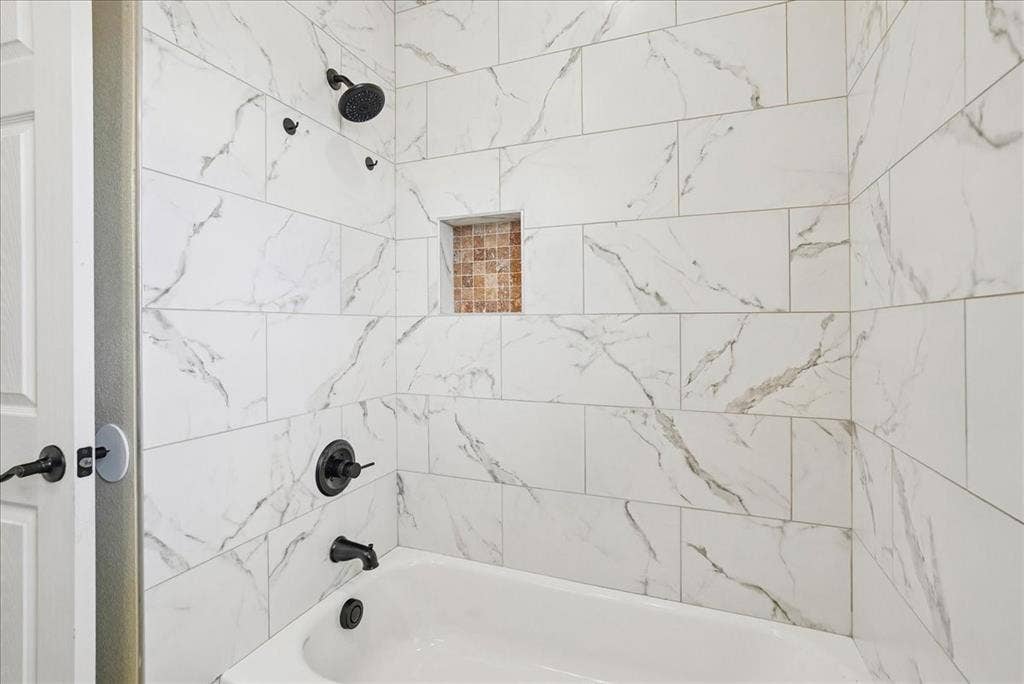 9060 Mitchell Bend Court, Granbury, TX 76048 Shower enclosure featuring large-format veined tile surround, recessed mosaic niche, matte black fixtures, and a white soaking tub