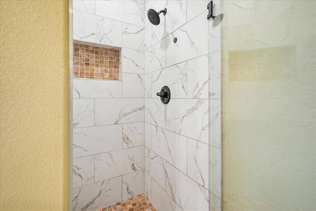 9060 Mitchell Bend Court, Granbury, TX 76048 Walk-in shower featuring large-format veined wall tile, mosaic tile floor and recessed niche, matte black fixtures, and a glass door