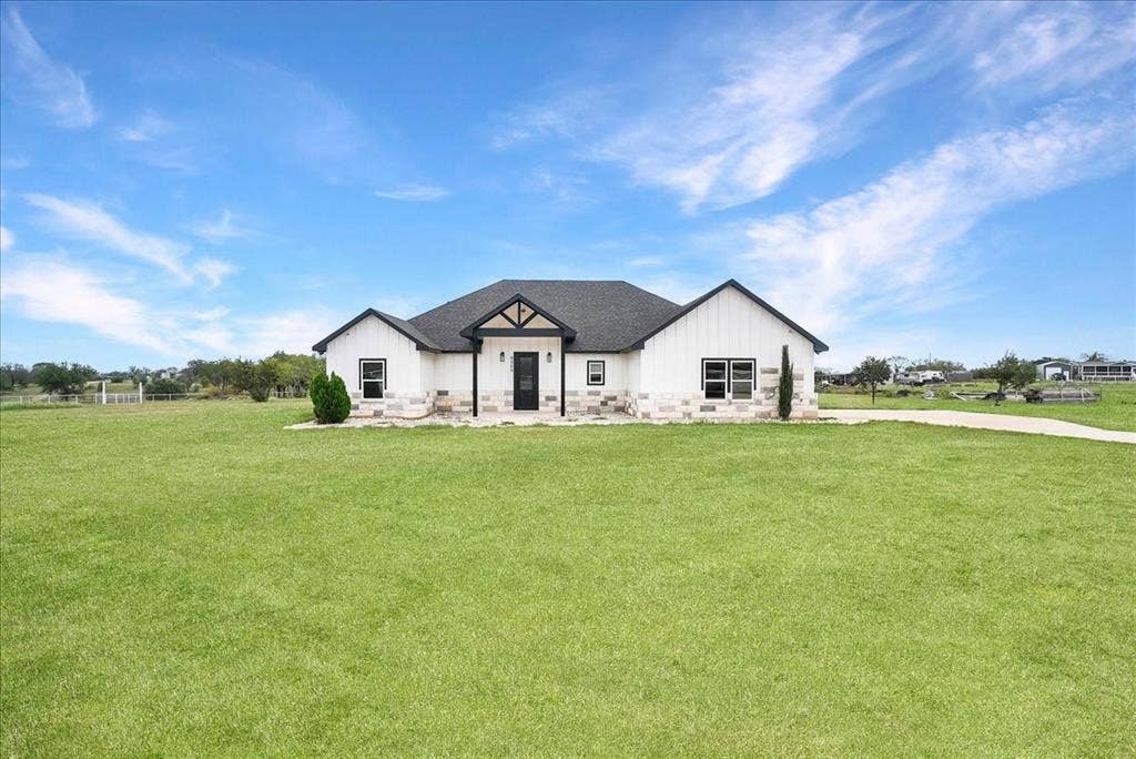 9060 Mitchell Bend Court, Granbury, TX 76048 Single-story residence featuring white board-and-batten siding, stone masonry wainscoting, an asphalt shingle roof, and a covered front entryway