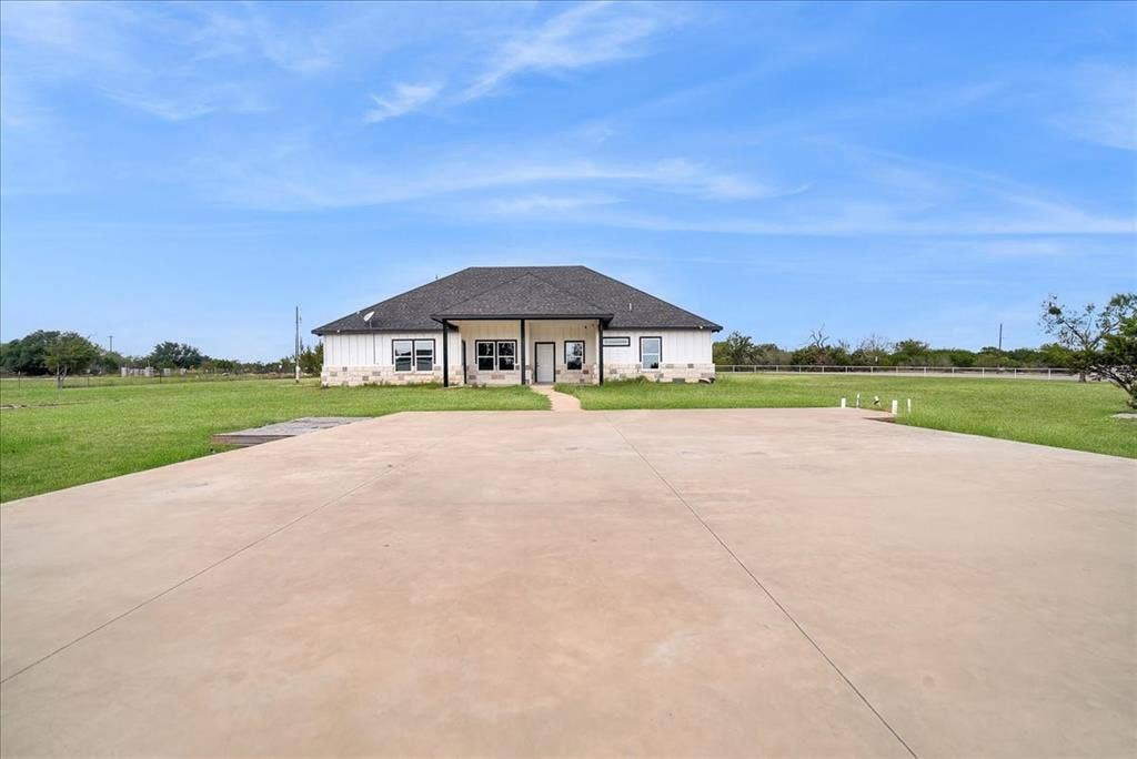 9060 Mitchell Bend Court, Granbury, TX 76048 Single-story exterior featuring a stone and board-and-batten facade, a dark shingled hipped roof, a covered front entryway, and an expansive concrete parking area