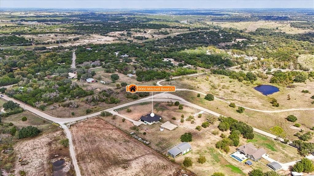 9060 Mitchell Bend Court, Granbury, TX 76048 Aerial perspective featuring expansive acreage, a circular driveway, a detached outbuilding, and mature trees on the property grounds