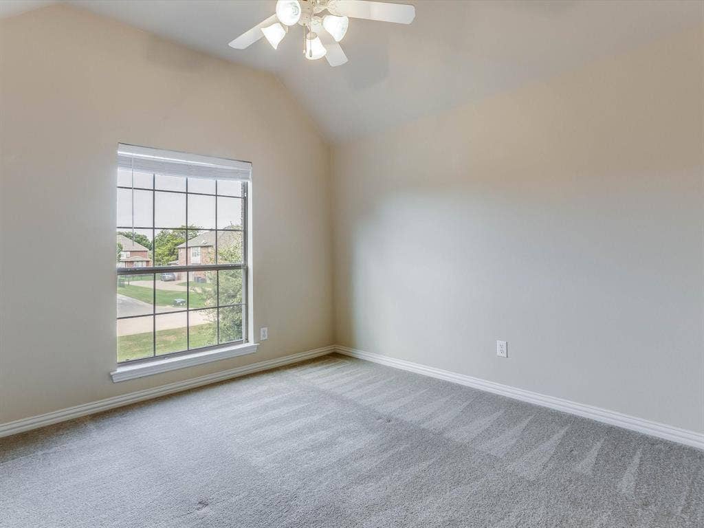 Vaulted ceiling featuring a central multi-light fan, large multi-pane window, and wall-to-wall carpeting