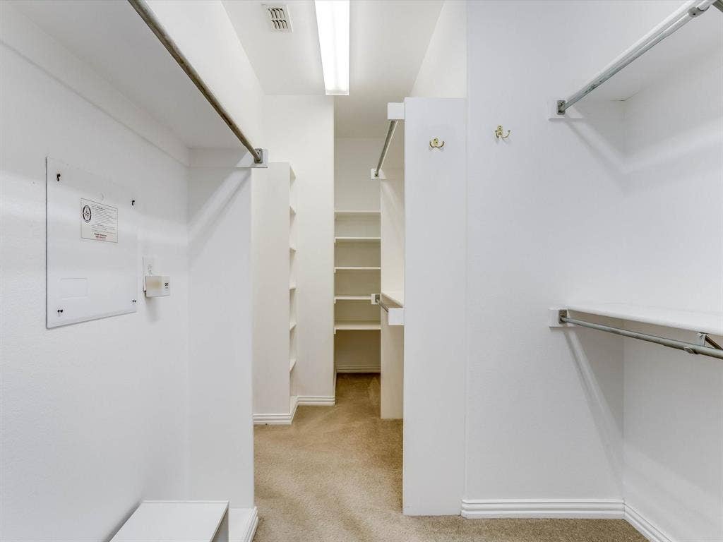 Walk-in closet featuring tiered clothing rods, integrated shelving units, and mounted garment hooks