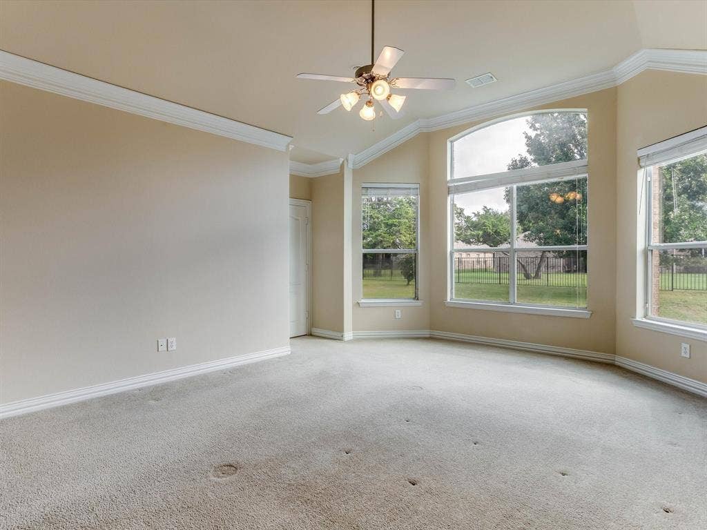 Vaulted ceilings featuring multi-tiered crown molding, expansive windows with arch-top detailing, and a central ceiling fan with multi-light fixture