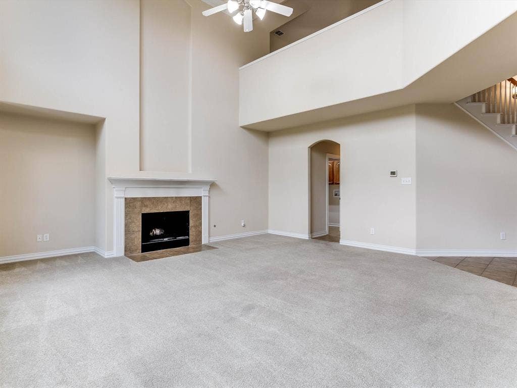 High-ceiling living area featuring a neutral color palette, a floor-to-ceiling architectural niche, a fireplace with a stone-tile surround and mantel, and an overlook with a staircase