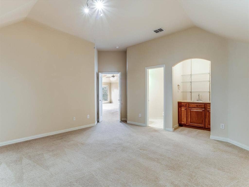 Vaulted ceilings, carpeted flooring, and a built-in wet bar featuring wood cabinetry, a sink, and glass shelving