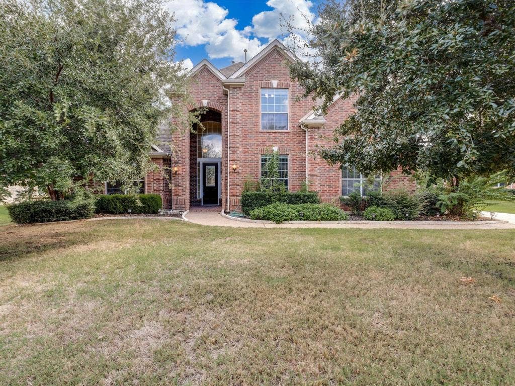 Multi-level brick exterior featuring a steeply pitched roofline, arched entryway, multi-pane windows, and mature landscaping