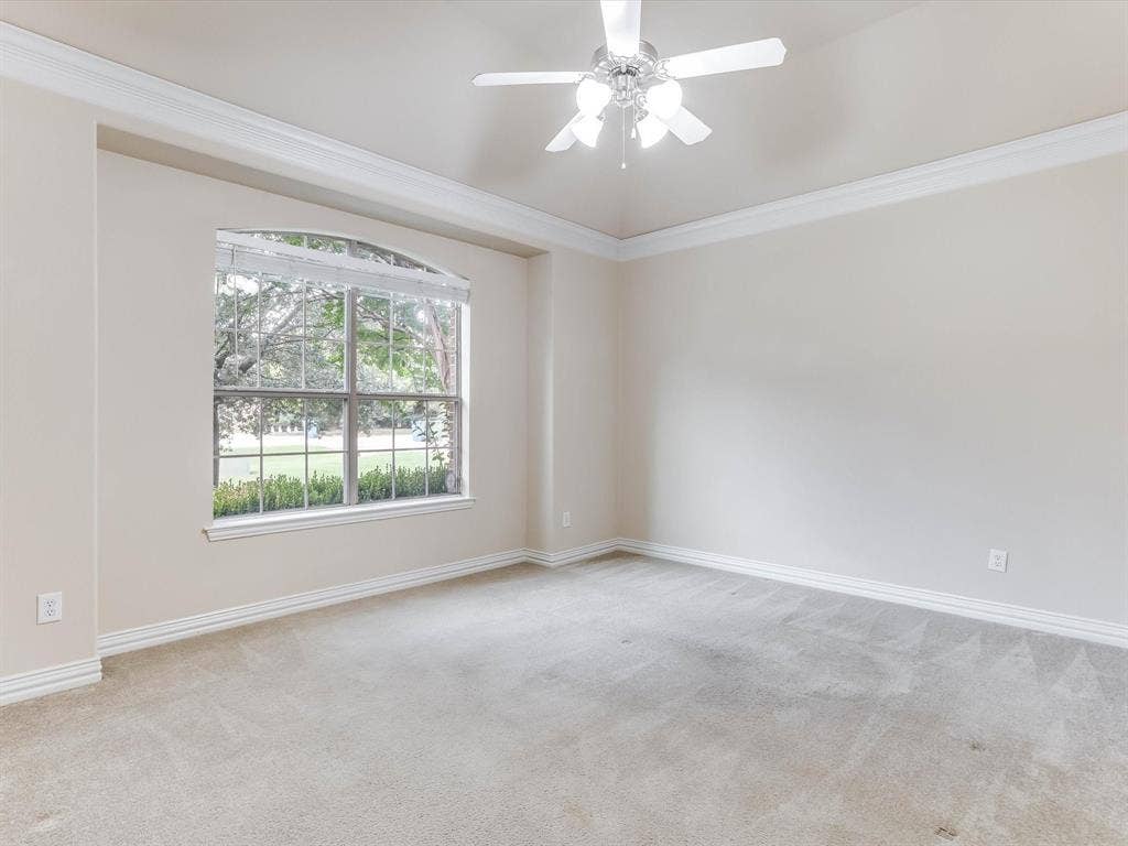 Tray ceiling with crown molding, arched window, and central ceiling fan