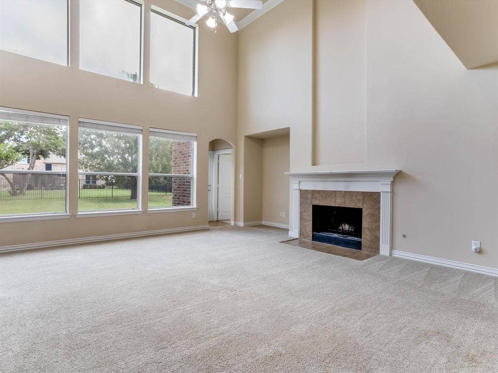 High-ceilinged room featuring expansive floor-to-ceiling windows, a fireplace with a white mantel and tile surround, and a ceiling-mounted light fixture