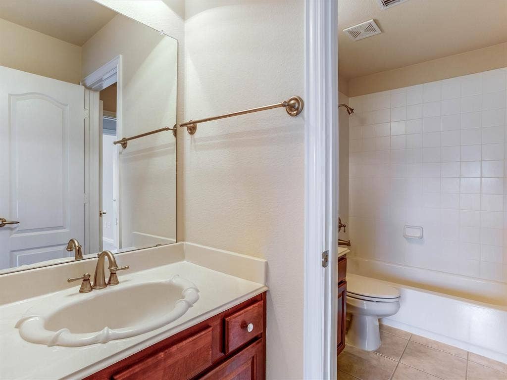 Bathroom featuring wood-finish cabinetry, a white countertop with an integrated basin, brass-tone hardware, a wall-mounted mirror, and a tiled tub-shower combination